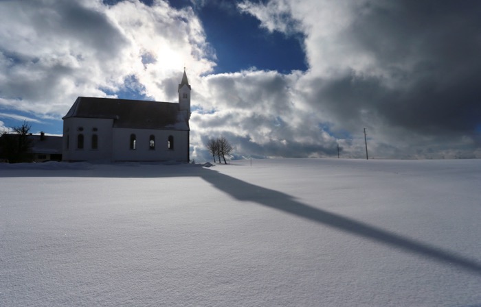 29 January 2019, Bavaria, Aitrang: The tower of the pilgrimage church Sankt Alban casts a long shadow in the sunshine on the freshly fallen snow. Photo: Karl-Josef Hildenbrand/dpa